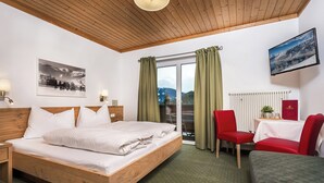 Habitación de hotel con cama de madera, un escritorio con silla, vista de montañas a través de la ventana y televisor montado.