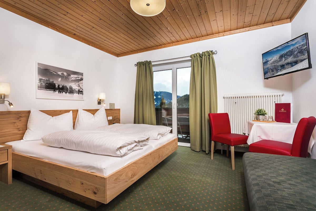 Habitación de hotel con cama de madera, un escritorio con silla, vista de montañas a través de la ventana y televisor montado.