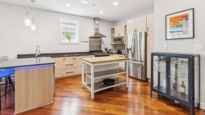 Ett modernt kök med träskåp, vitvaror i rostfritt stål, en köksö och ett vinskåp.