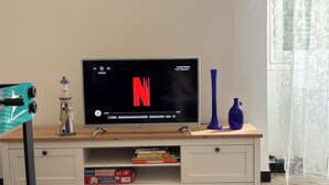 A television on a wooden TV stand with a decorative lighthouse and vases. - Three-room apartment just a few steps from the beaches in the center of Imperia (Imperia)