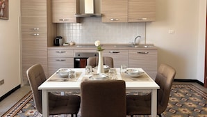 A modern kitchen with light wood cabinetry, a central island, and a dining area with four chairs and a table set for four. - Three-room apartment just a few steps from the beaches in the center of Imperia (Imperia)