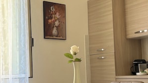 A dining area with a table set for four, a vase with a single white rose, and a painting of flowers on the wall. - Three-room apartment just a few steps from the beaches in the center of Imperia (Imperia)