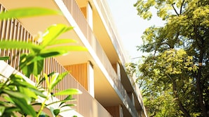 Un edificio moderno con estructura de varios pisos, balcones y vegetación circundante.