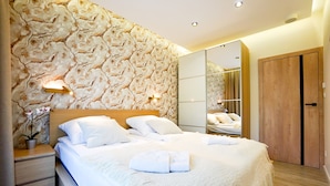 Un dormitorio moderno con pared de diseño de mármol, cabecera de madera, cama grande con ropa de cama blanca, mesita de noche con una planta y un armario.