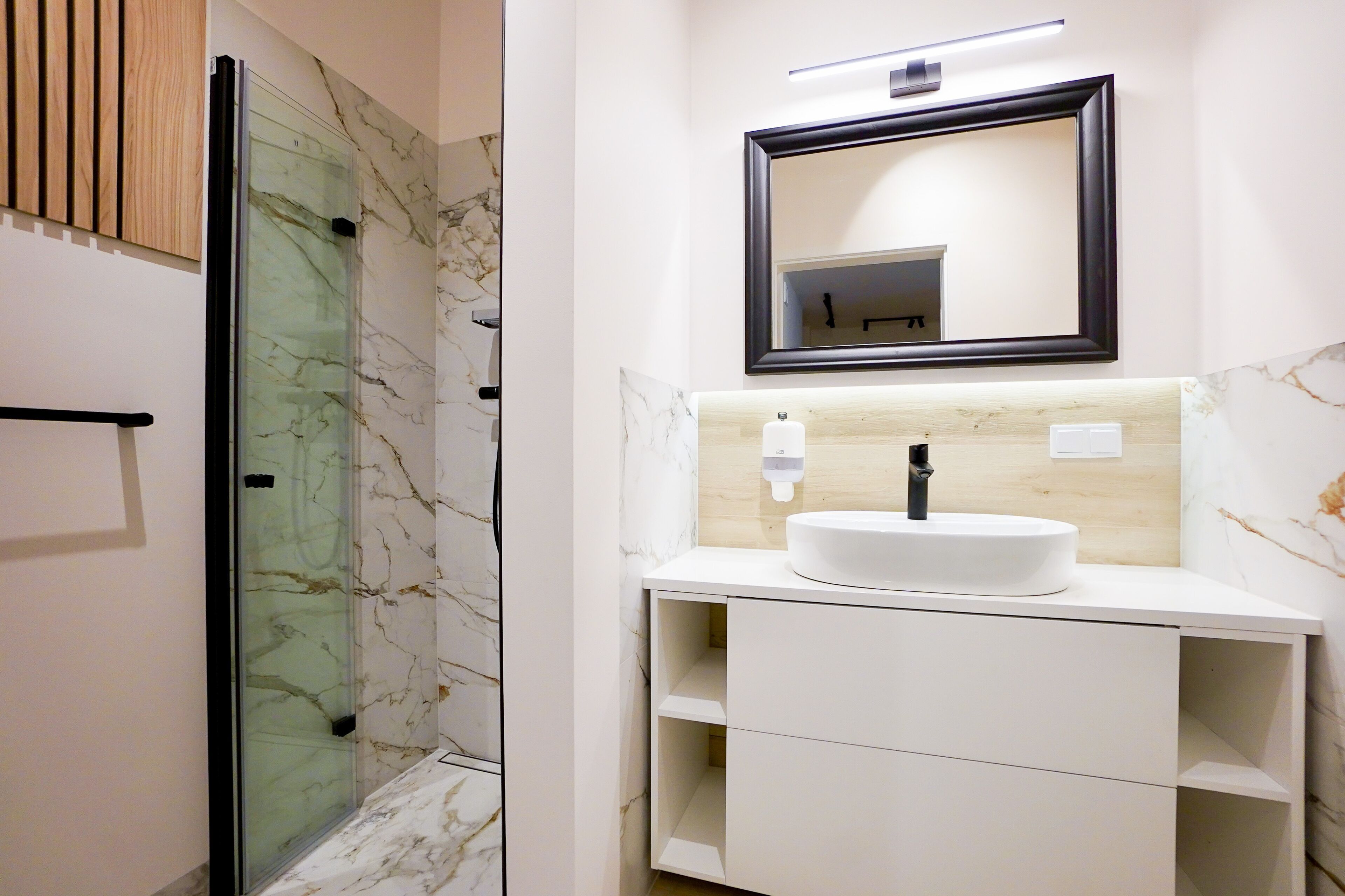 A modern bathroom with a glass shower enclosure, a white sink with a marble countertop, and a wooden cabinet.