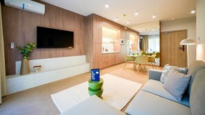 Una sala de estar moderna con un televisor de pantalla plana, un sofá, un comedor con sillas y una cocina al fondo.