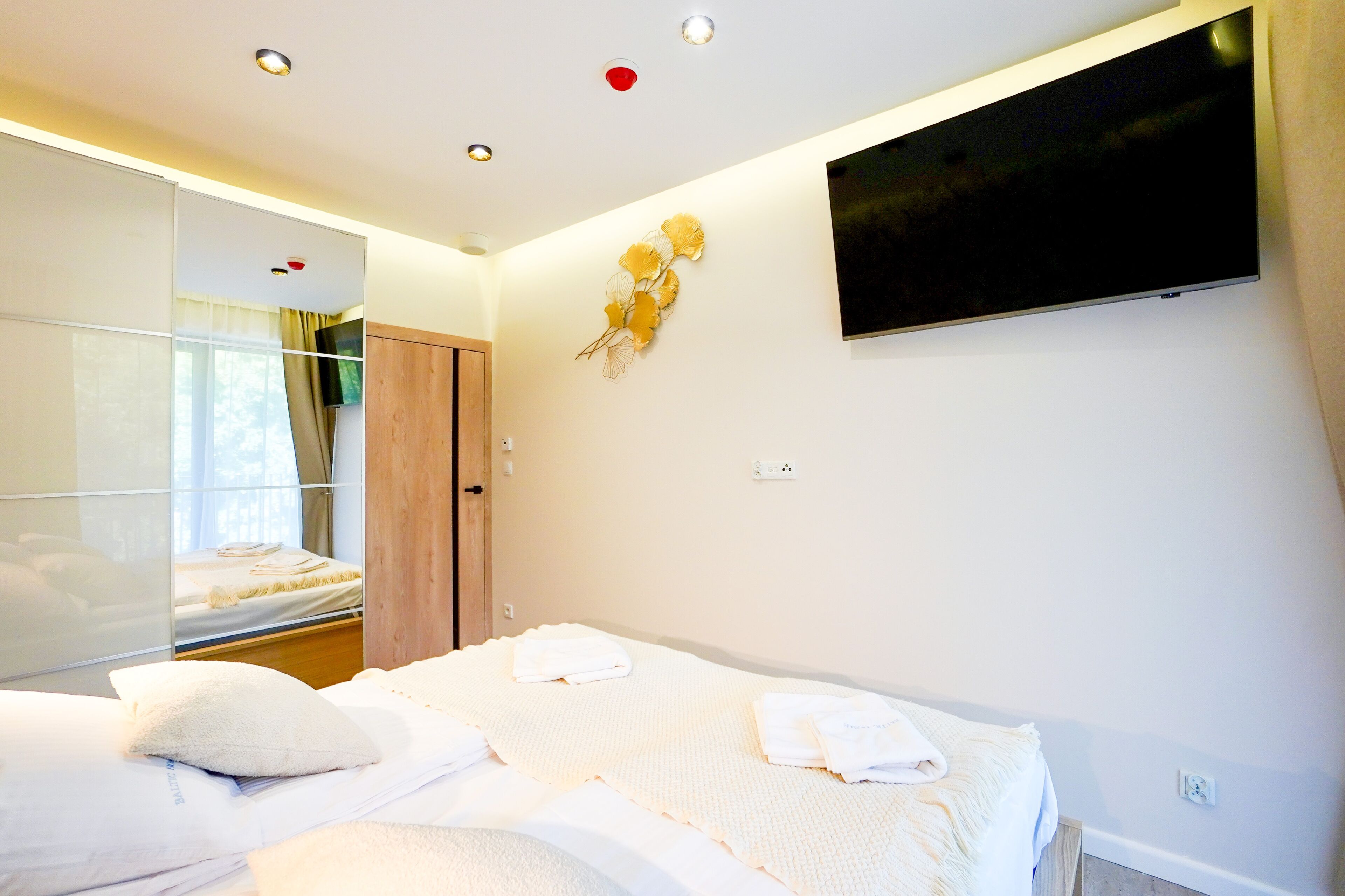Une chambre d’hôtel avec un lit, un téléviseur fixé au mur et un miroir qui reflète une partie de la pièce.