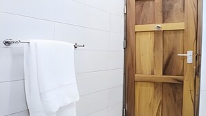 Un baño con paredes de azulejos blancos, una puerta de madera y una toalla colgada en un perchero de metal.