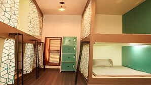 Habitación con literas, piso de madera, un armario verde y una ventana con persianas.