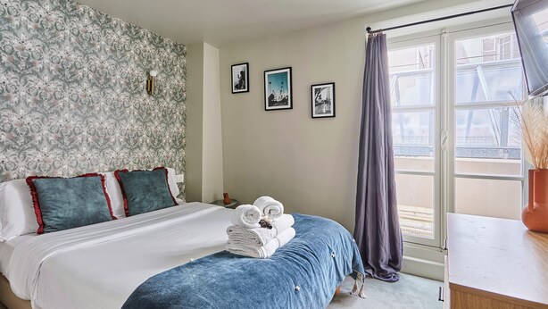 A hotel room with a bed, a window with curtains, and three framed pictures on the wall. - Charming Studio Center of Paris (Paris)