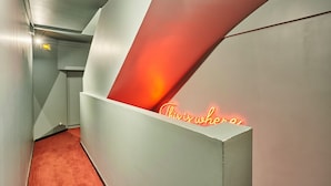 A modern hallway with a red carpet, a neon sign reading "This is who," and a white wall with a geometric design. - Charming Studio Center of Paris (Paris)
