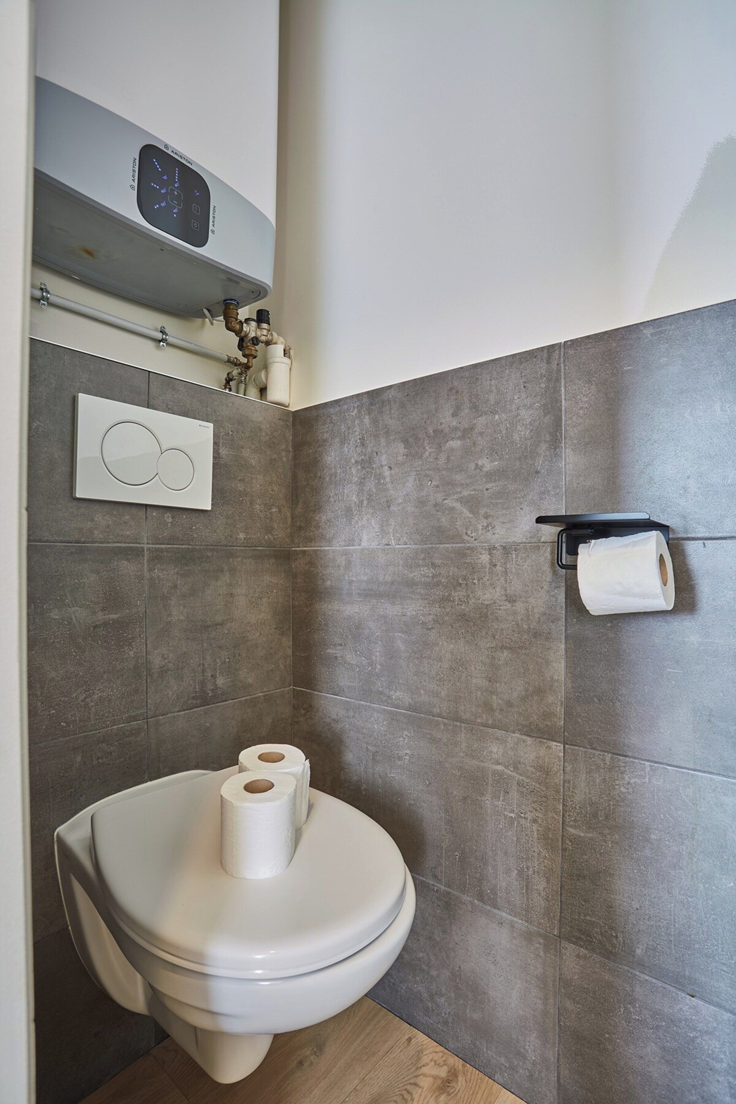 Een moderne badkamer met een toilet, een toiletrolhouder aan de muur en een zichtbare boiler.