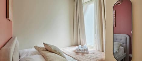 A bedroom with a bed, pillows, a bedside table, a mirror, and a window with curtains.