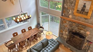 Un comedor con una mesa y sillas de madera, una araña y una chimenea de piedra con un cuadro enmarcado encima.
