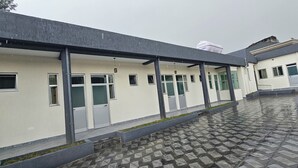 A covered outdoor area with a tiled floor, multiple doors, and a building with a flat roof. - Cozy villa (Addis Ababa)