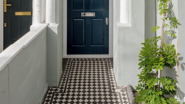 Een wit gebouw met een donkerblauwe deur, witte zuilen en een zwart-wit geruite vloer.