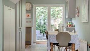 Een keuken met een eethoek, een klok en uitzicht op de tuin.