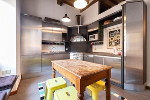 A modern kitchen with stainless steel appliances, a wooden table, and yellow stools.