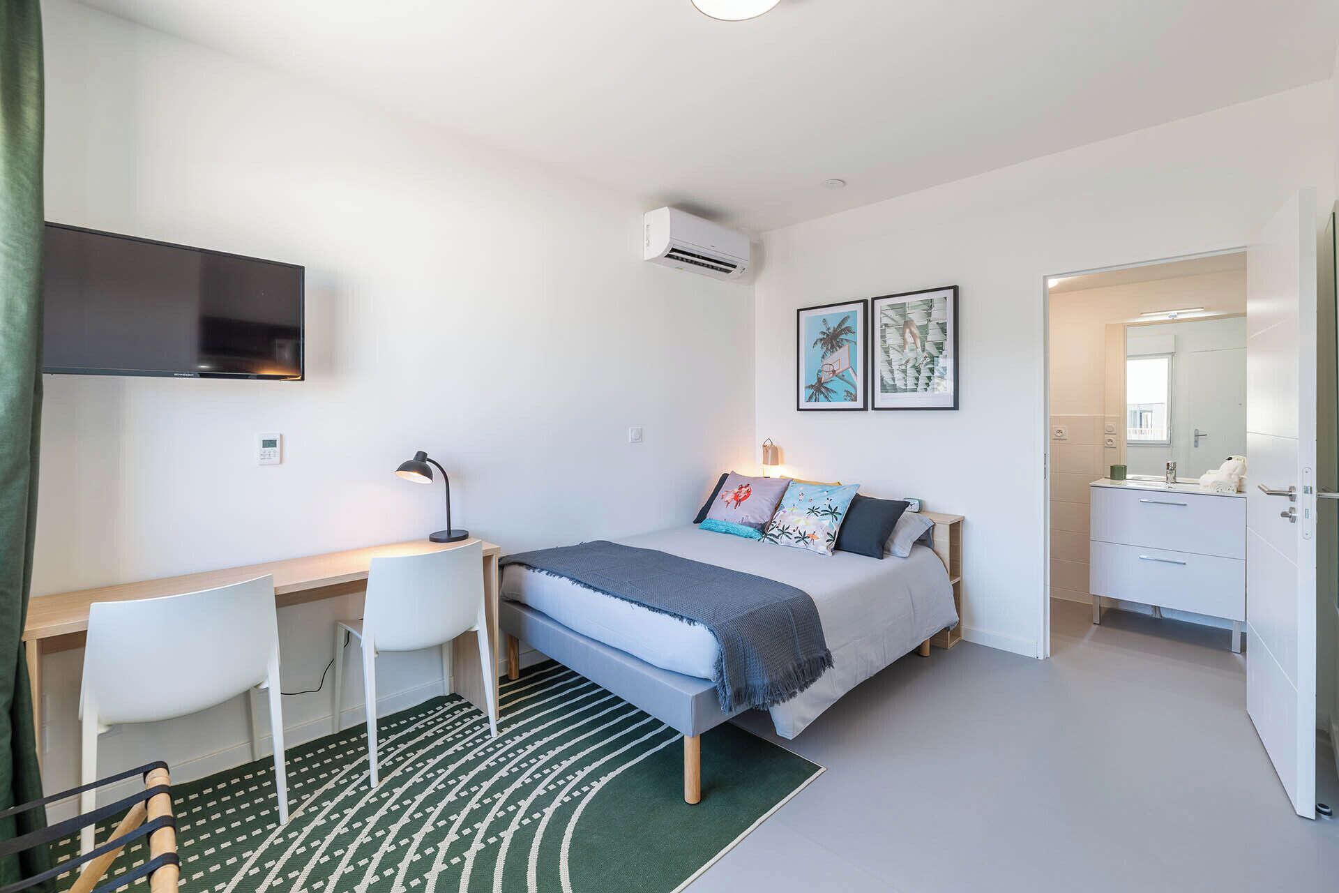 A modern bedroom with a bed, desk, chair, and a TV mounted on the wall.
