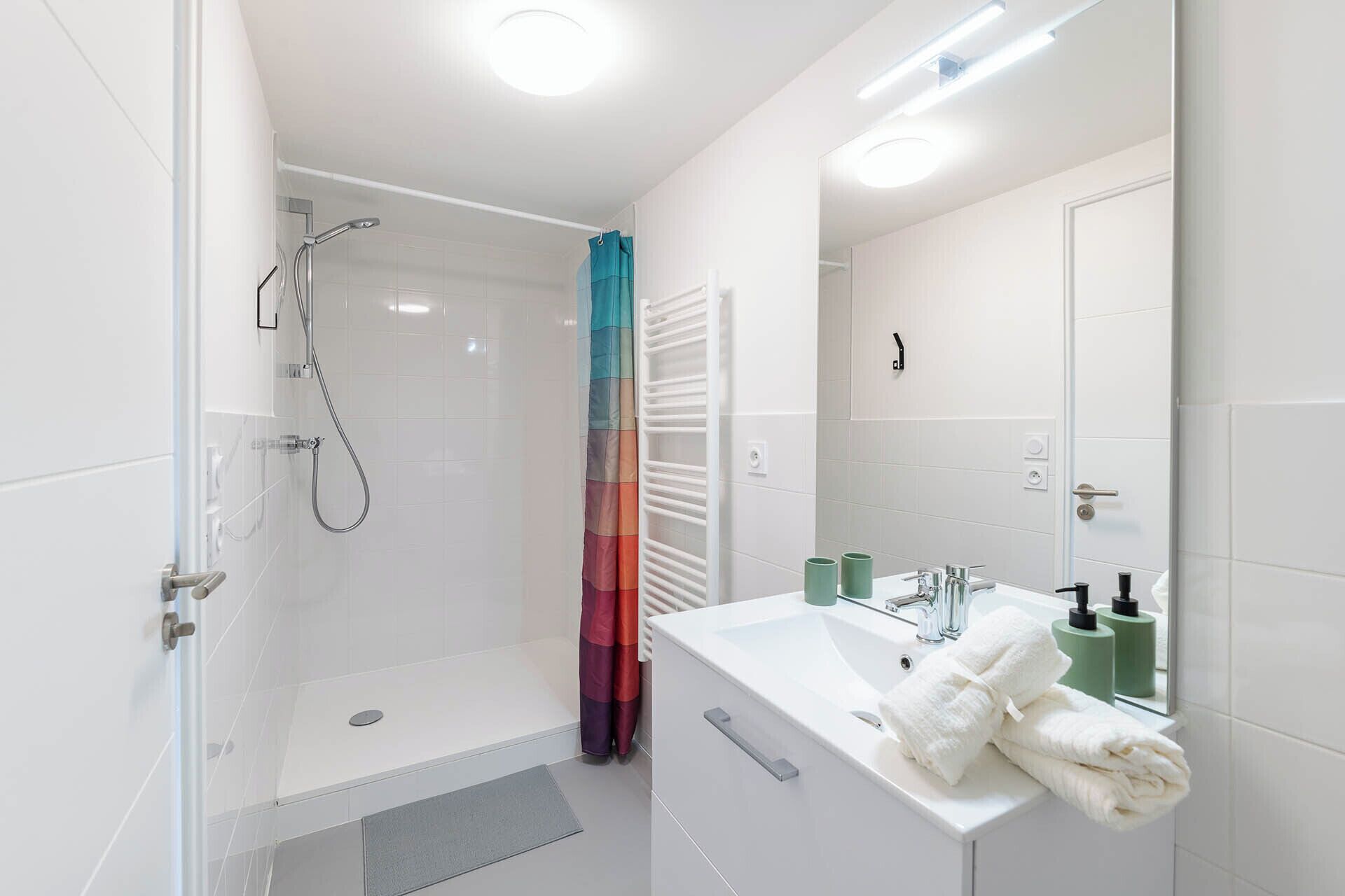 A modern bathroom with a shower, a sink with a mirror, and a towel rack.