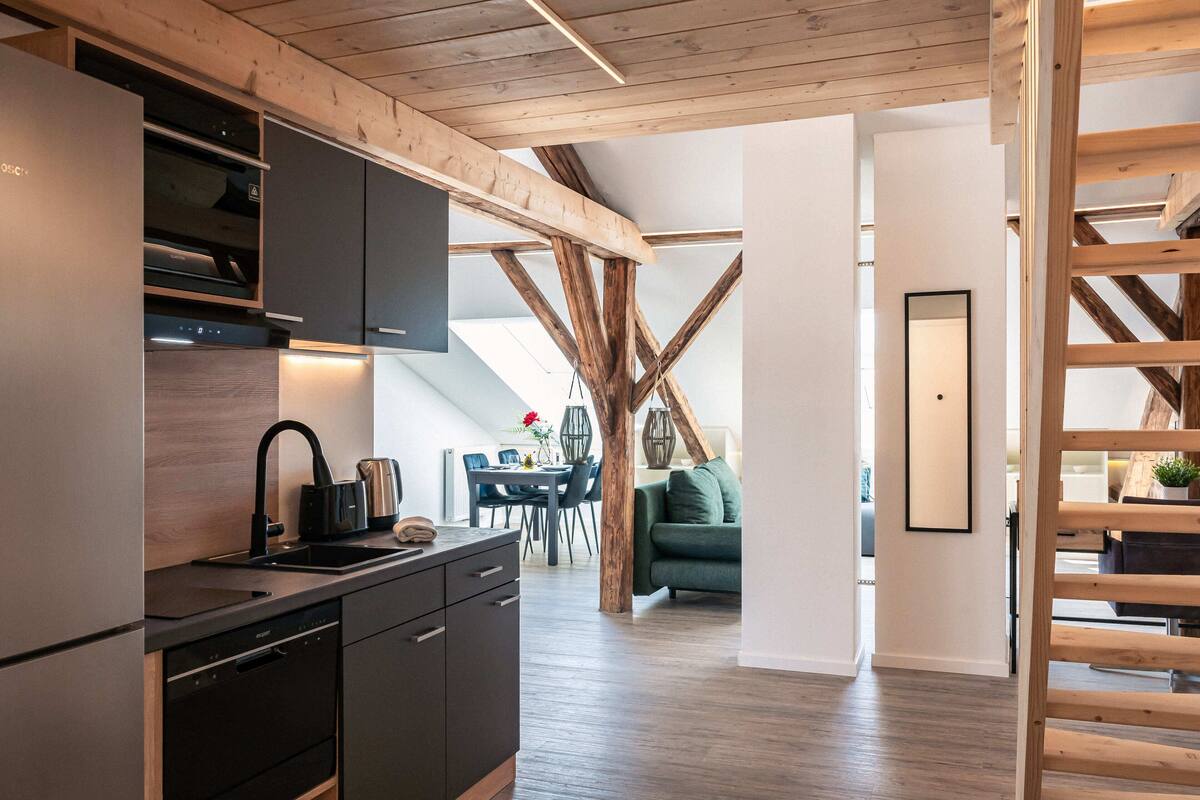 A modern kitchen with built-in appliances, wooden beams, and a dining area with a green sofa.