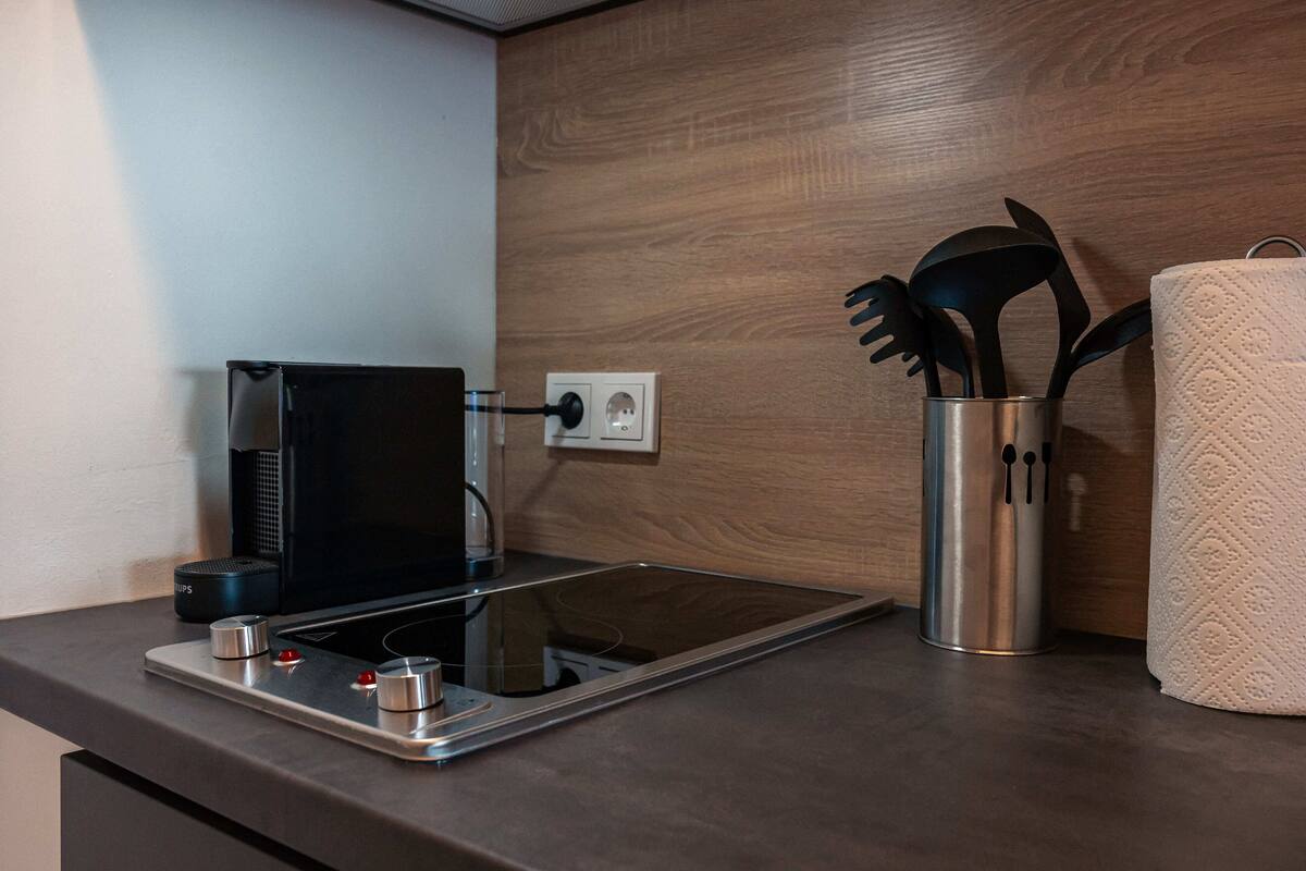 A modern kitchen with a built-in microwave, a kettle, and a stainless steel container holding kitchen utensils.