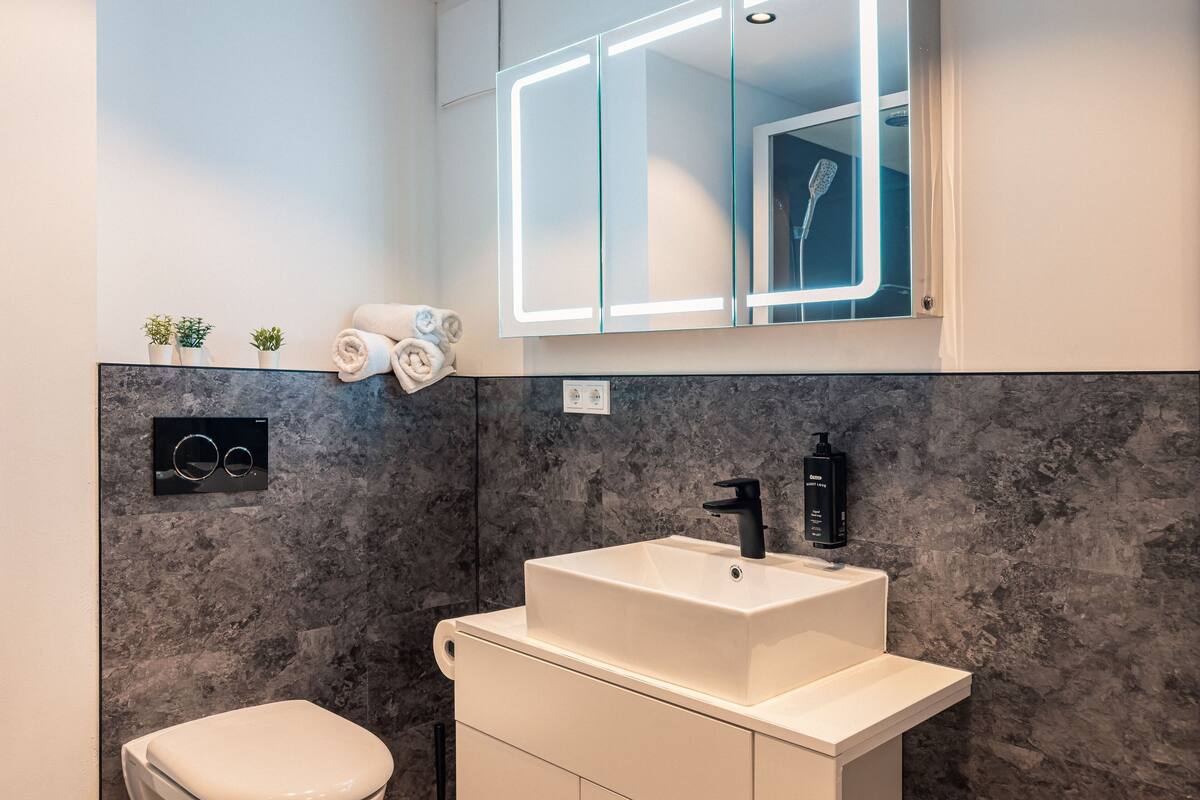 A modern bathroom with a marble backsplash, a white sink, a black faucet, and a glass-enclosed mirror.