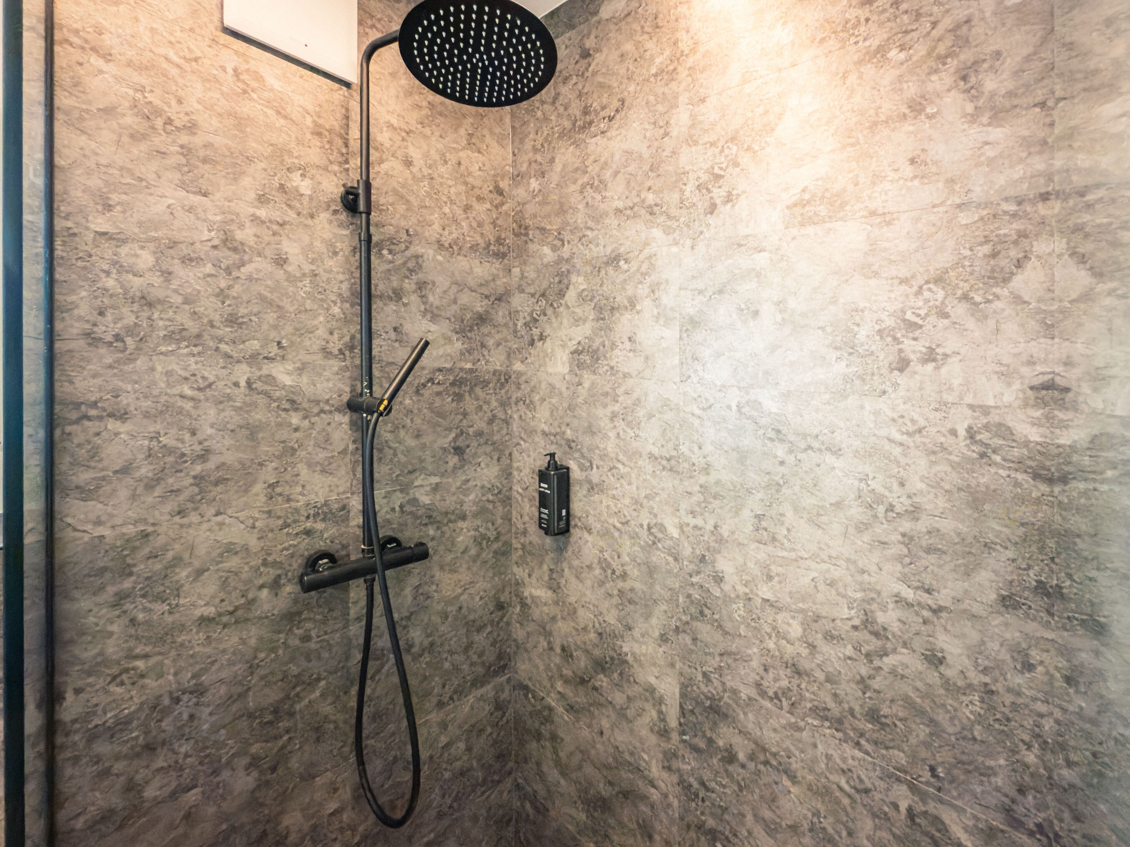 Ducha con cabezal de mano, plato de ducha y panel de control en una pared con relieve.