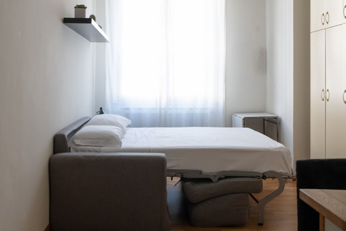 Une chambre à coucher comprenant un lit, une table de chevet, une chaise, une petite étagère avec des plantes et une armoire.