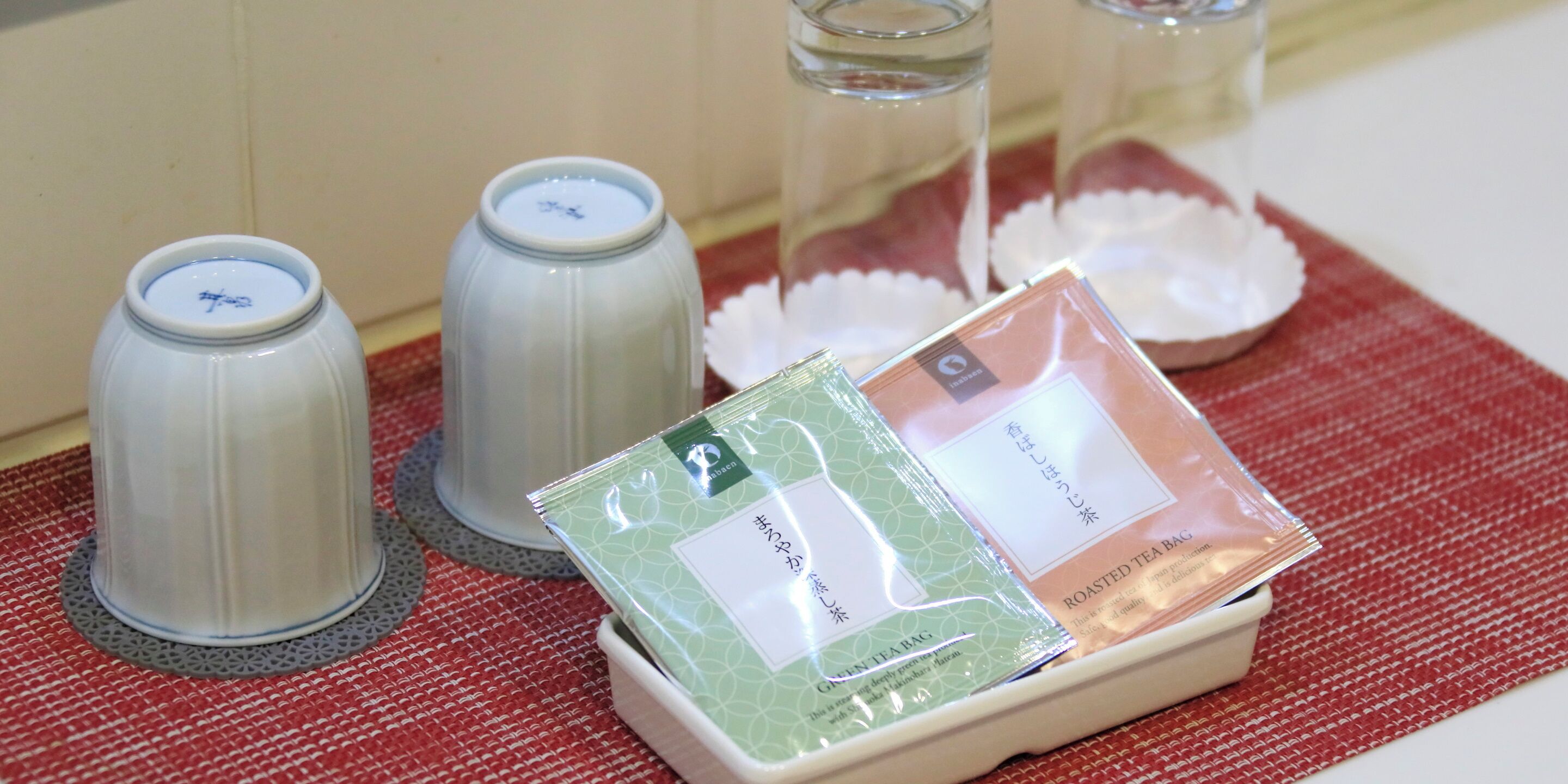 A tray with tea bags and a teapot on a red mat.