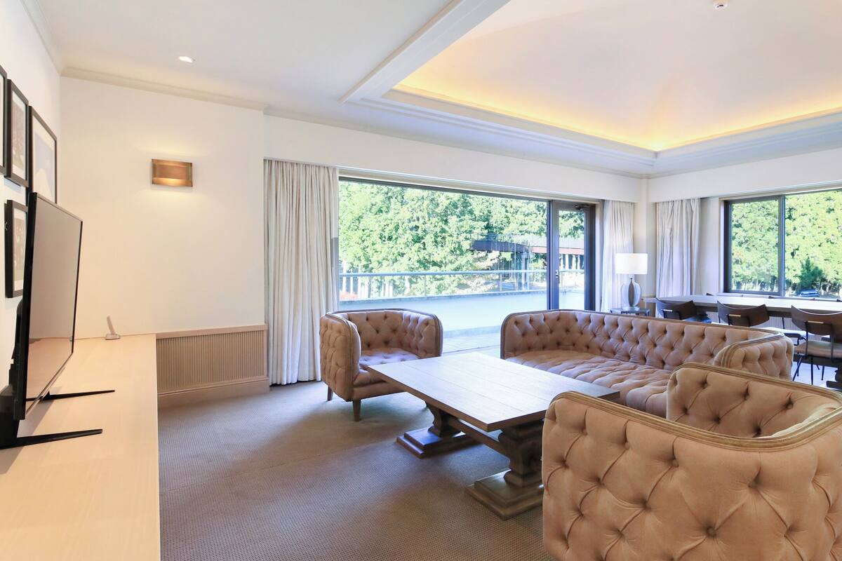 A spacious room with a large sectional sofa, a dining table, and a television.