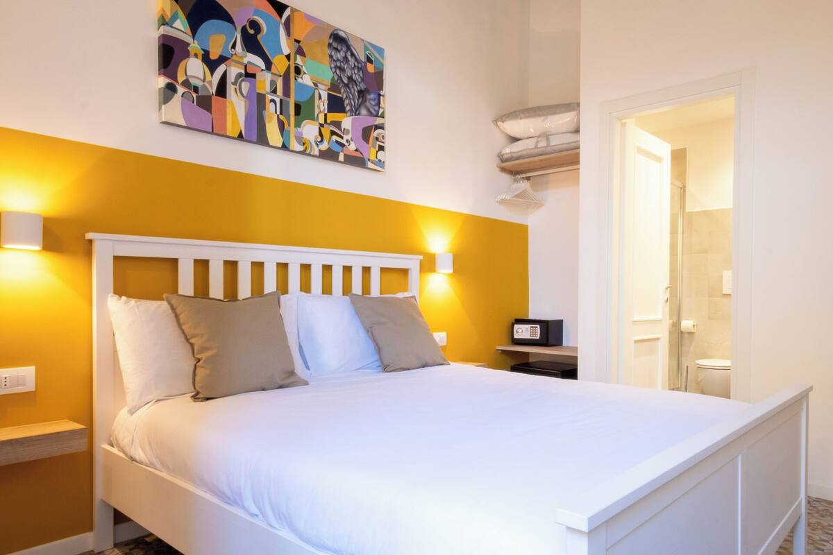 Habitación de hotel con una cama blanca, una pared de acento amarilla y un cuadro sobre la cama.