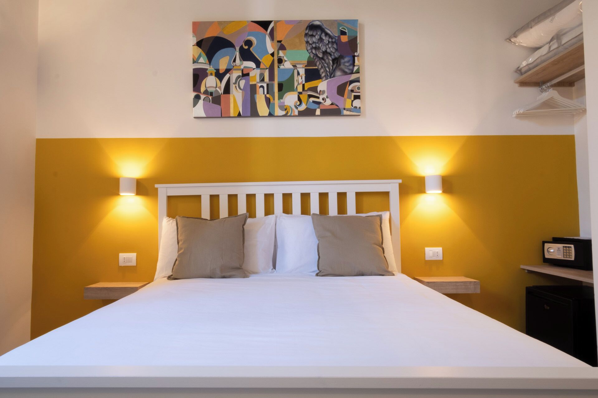 A bed with a white headboard, two bedside lamps, and a painting above it.