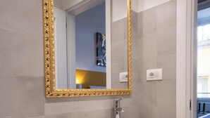 A modern bathroom with a round white sink, a gold-framed mirror, and a wooden vanity. - Decumano 43  (Naples)
