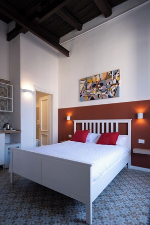 A bedroom with a white bed, red pillows, a modern abstract painting, and patterned floor tiles. - Decumano 43 (Naples)