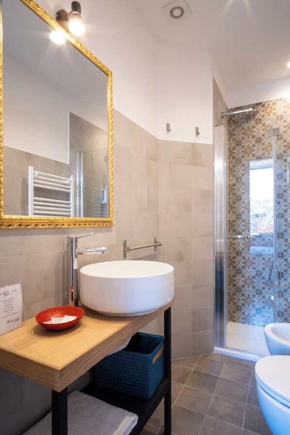 A modern bathroom with a large mirror, a white sink, and a shower area. - Decumano 43 (Naples)