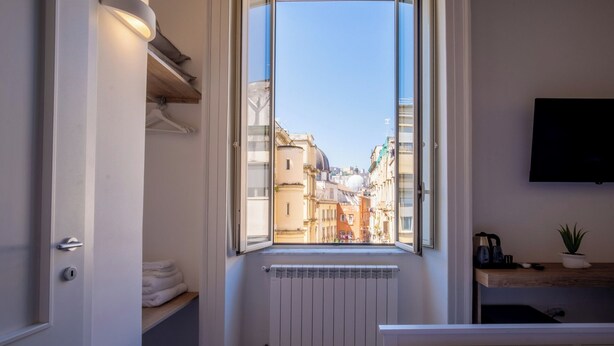 A hotel room with a large window, a bed, a radiator, a TV, and a shelf with towels. - Decumano 43  (Naples)