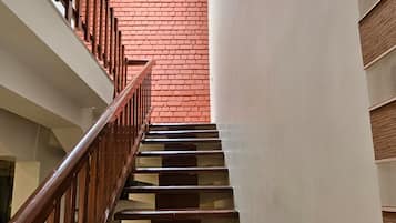 A staircase with wooden handrails and steps, leading to a room with a red brick wall and a skylight.