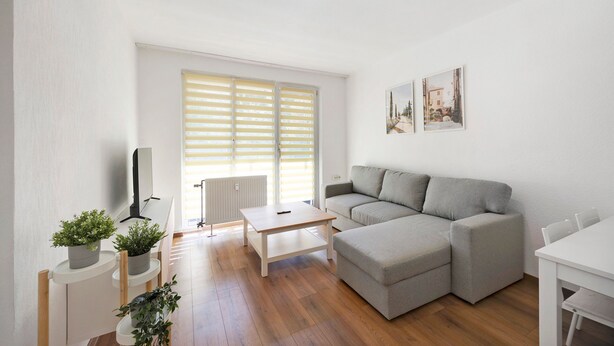 En opholdsstue med sofa, sofabord, fjernsyn og potteplanter.