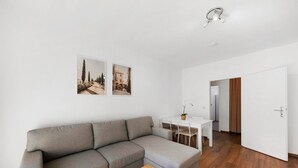 En moderne stue med en grå sofa, et træbord og et spiseområde med et hvidt bord og stole.