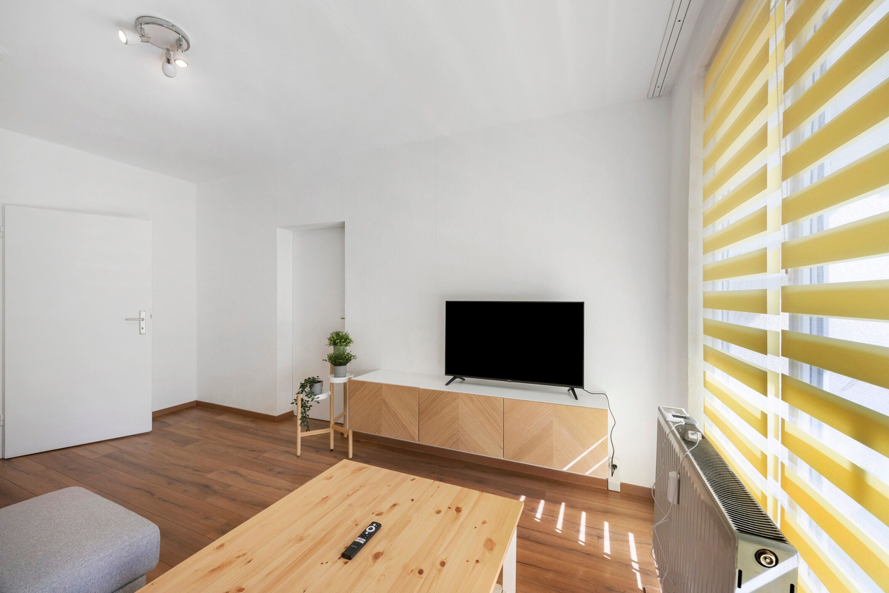 A modern living room with a flat-screen TV, wooden flooring, a small table, and a radiator.