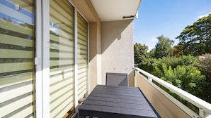 En balkon med et bord, en skydedør og udsigt til grønne områder.