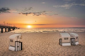 A beach with two beach chairs labeled U30 and U29, a pier in the background, and the sun setting over the ocean.