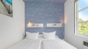 A bedroom with a bed, two pillows, a nightstand with a lamp, and a window with a view of greenery. - Quiet bungalow in Bansin with garden & WLAN - suitable for families & dogs (Seebad Bansin)
