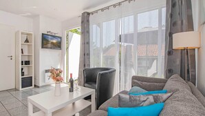 A modern living room with a sofa, a coffee table, a TV, and a large window with curtains. - Quiet bungalow in Bansin with garden & WLAN - suitable for families & dogs (Seebad Bansin)