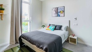 A modern bedroom with a large bed, a bedside table, a small nightstand, a window with curtains, and a wall-mounted picture. - Student Factory Nancy Centre (Nancy)