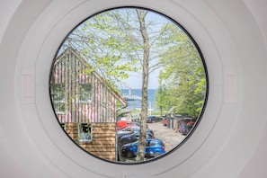A view through a circular window of a building with a brick facade, parked cars, and a body of water in the background.