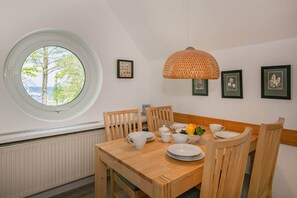 Et spiseområde med et rundt bord, træstole, en hængende lampe og billeder i rammer på væggen.