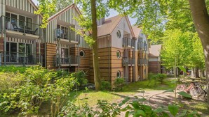 Un immeuble résidentiel doté de nombreux balcons, d’un jardin agrémenté d’arbres et d’arbustes, et d’un vélo garé à l’extérieur.