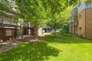 A courtyard with a brick building, a tree-lined pathway, and a grassy area.